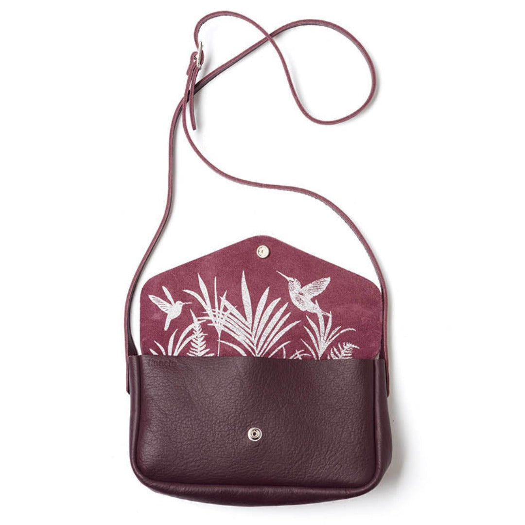 Din nye burgunder crossbody-veske i skinn har plass til alt du trenger! Elegant med kolibri- og tropiske blader-trykk på innsiden. Mål:27cm x 16cm x 7cm.