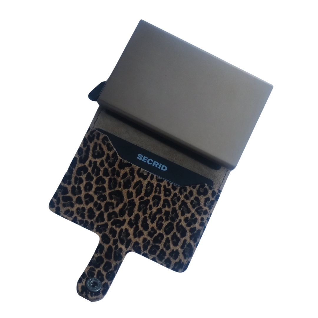 Miniwallet kombinerer det beste fra to verdener. Skallet rommer sedler, kvitteringer og kort, kortbeskytteren i aluminium lar kort skyves ut med en enkel bevegelse og beskytter dem mot bøying, brudd og uønsket trådløs kommunikasjon. St.: 65x102x21 mm. Vekt: 72 gram. Farge: leopard-beige. Leveres i en gaveeske.