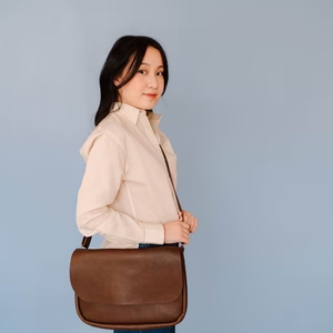 Person som bærer en brun skulderveske i skinn over skulderen, sett fra siden.